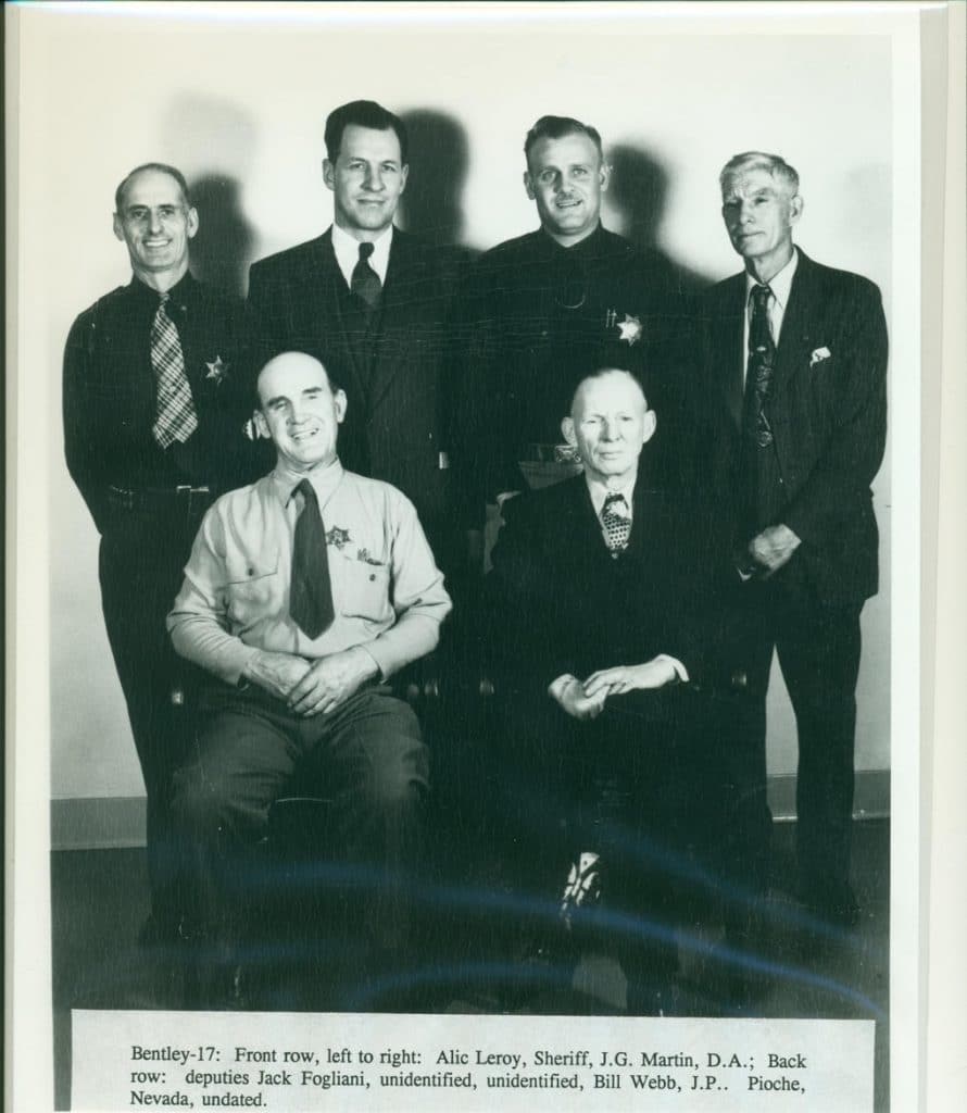 Six men, some in uniform, pose for a group photo; two are seated, four stand behind them.