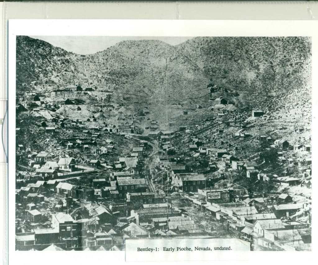 A black and white photo shows a mining town with many buildings nestled in a valley between two hills.