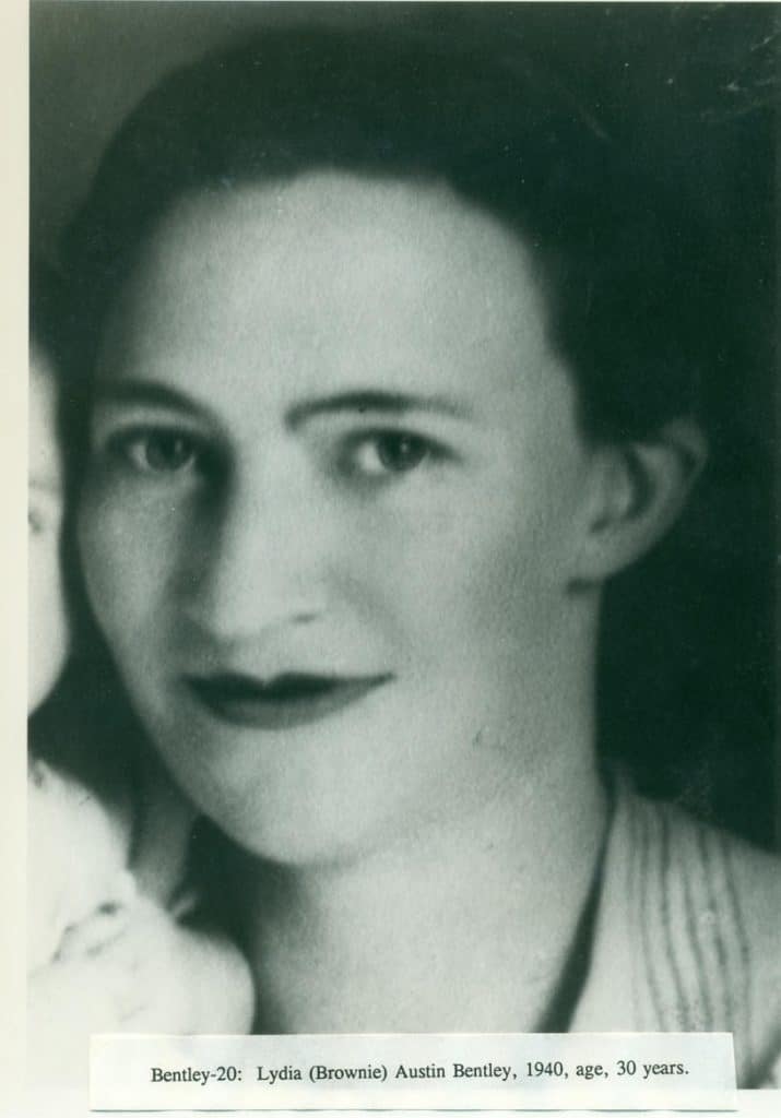 A black and white portrait shows a woman with dark hair, dark eyes, and dark lipstick, looking forward.