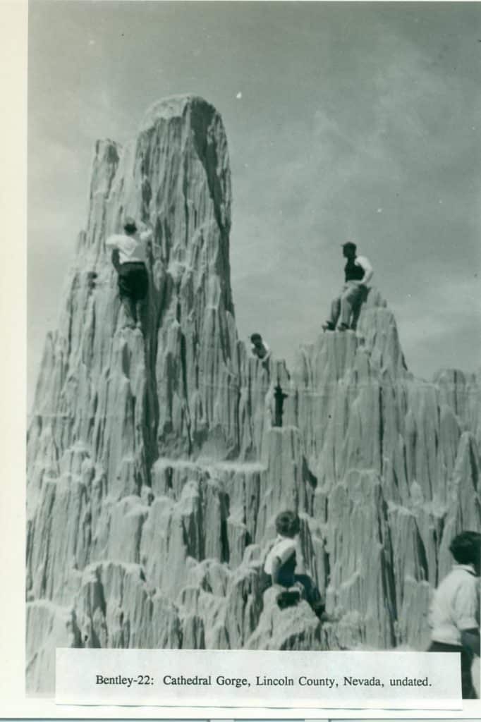 A black and white photo shows several people climbing and sitting on tall, eroded rock formations.