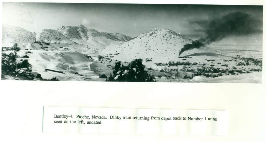 A panoramic black and white photo shows a snowy mountain landscape with a train and mining town.