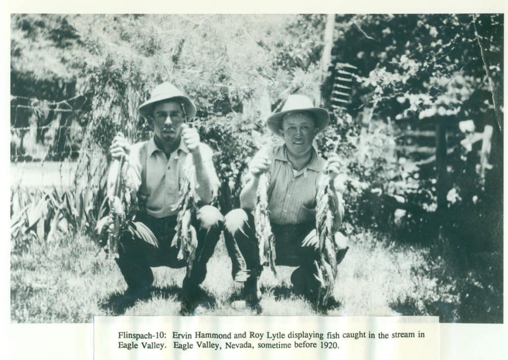 Two men in hats crouch, holding strings of fish, with "FLINSPACH-10: Ervin Hammond and Roy Lytle displaying fish caught in the stream in Eagle Valley, Nevada, sometime before 1920" at the bottom.