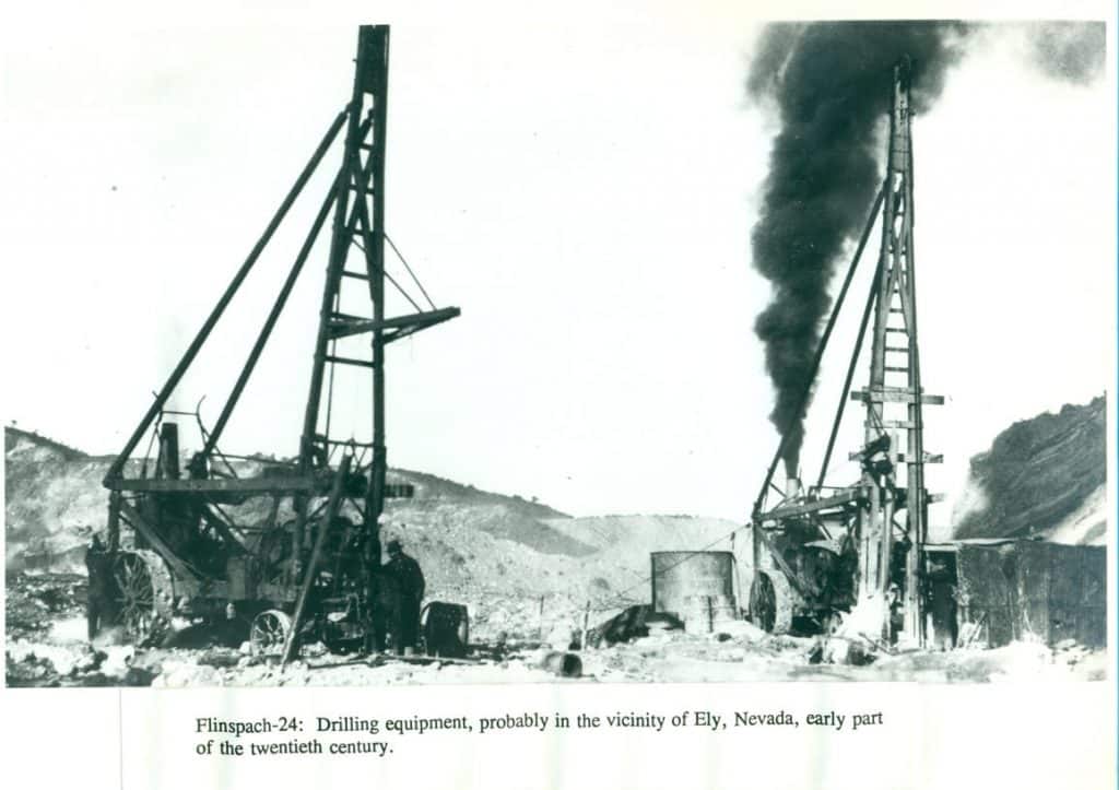 Two early 20th-century drilling rigs stand in a barren landscape, one on the right emitting thick black smoke.