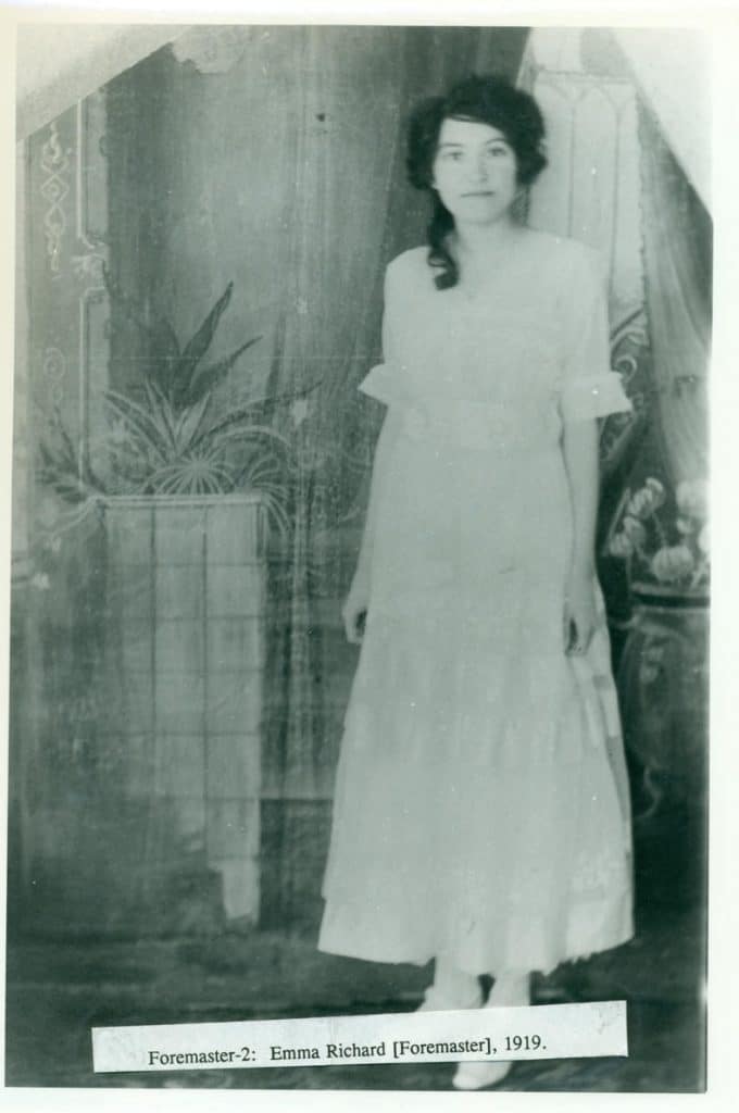 A young woman in a light-colored dress stands in front of a painted backdrop with plants; text reads "Foremaster-2: Emma Richard [Foremaster], 1919."