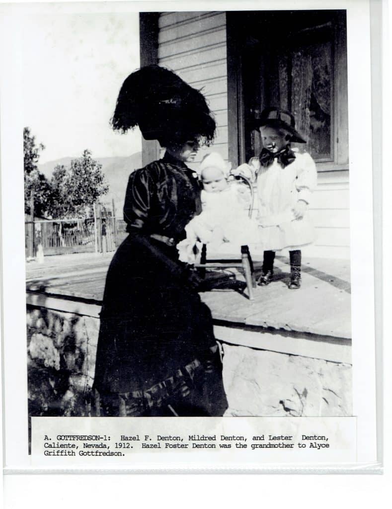 A black and white photo of a woman in a large hat holding a baby, with a child standing nearby.