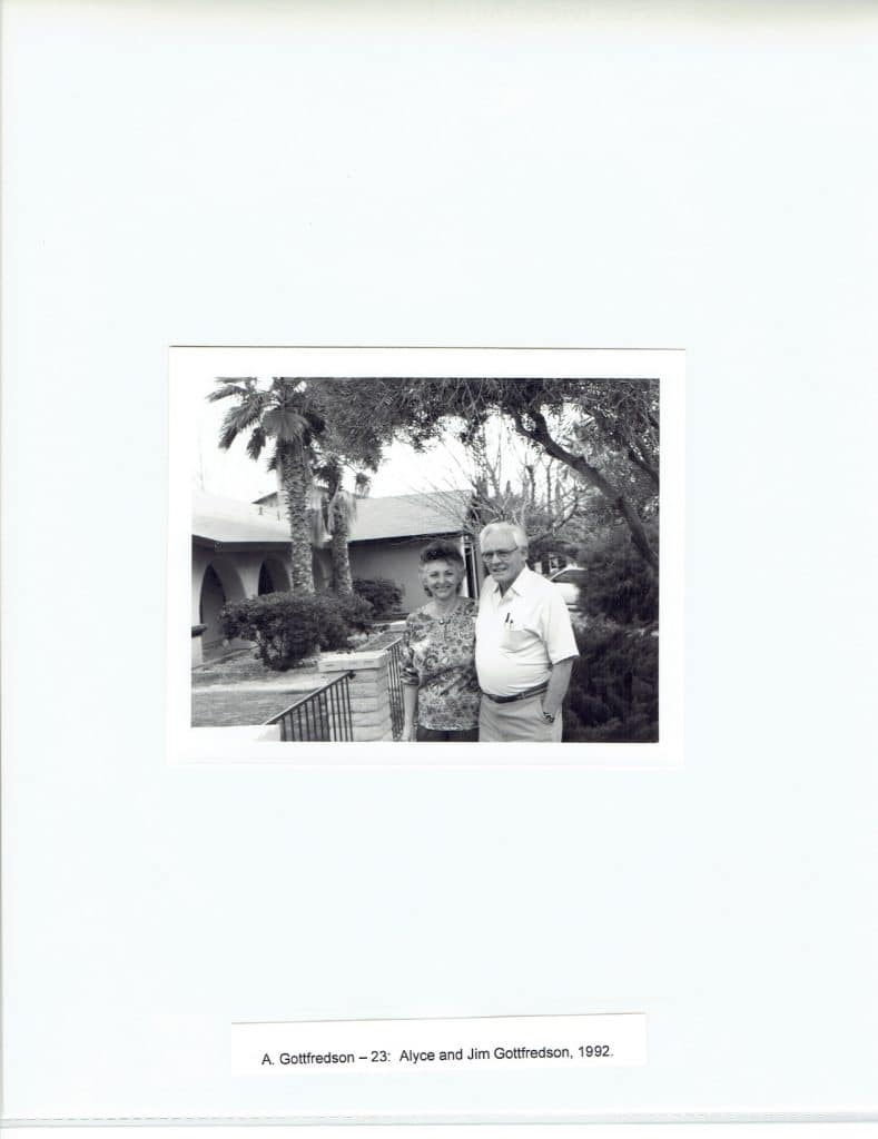 A black and white photo shows a man and woman smiling outdoors, with palm trees and a building behind them.