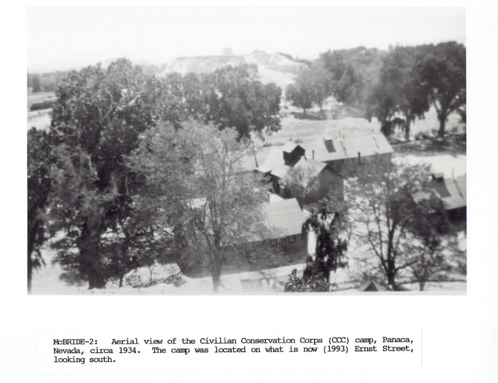 Black and white aerial view of a Civilian Conservation Corps camp with buildings among many trees.