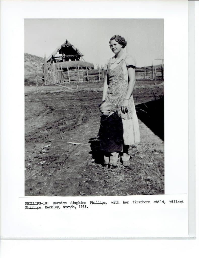 A black and white photo shows a woman in a dress and a small child standing in a dirt field.