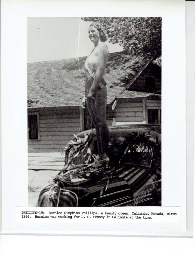 A smiling woman with short hair and a "MISS CALIENTE" sash stands atop a car with a house behind her.