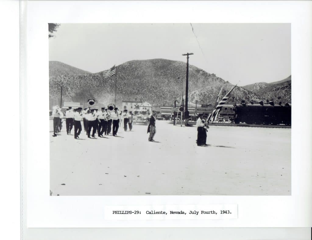 A black and white photo shows a marching band and large American flag in Caliente, Nevada, July 1943.
