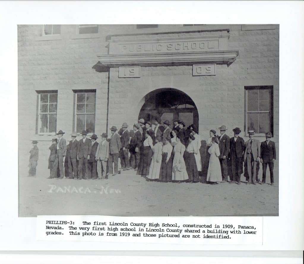 A black and white photo shows a large group of men and women standing outside a "PUBLIC SCHOOL" building.