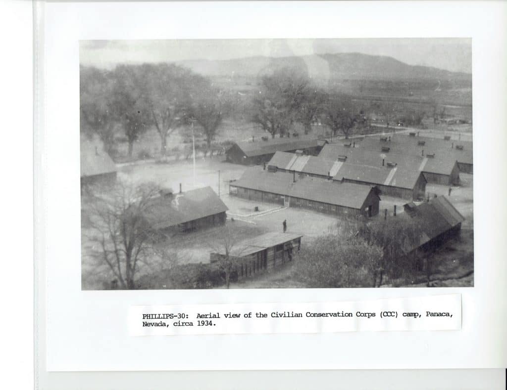 Black and white aerial view of a Civilian Conservation Corps camp with many barracks and trees.