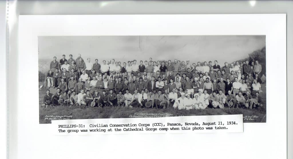 A large group of men, mostly in work clothes, pose for a photo with "PHILLIPS-31: Civilian Conservation Corps (CCC), Panaca, Nevada, August 21, 1934. The group was working at the Cathedral Gorge camp when this photo was taken." below.