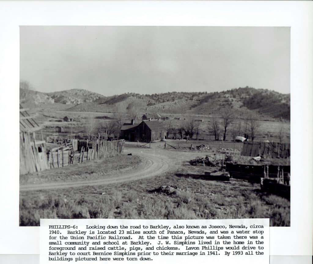 Black and white photo of a dirt road curving past a barn, fences, and sparse trees in a valley.