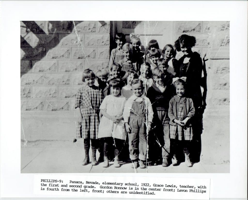 A black and white photo shows a teacher and 15 young children standing outside a brick building.
