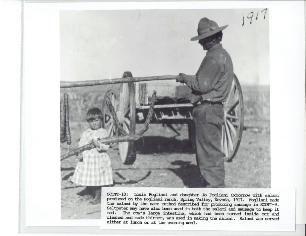 A man in a hat and a child in a dress hang salami on a stick, with "1917" written.