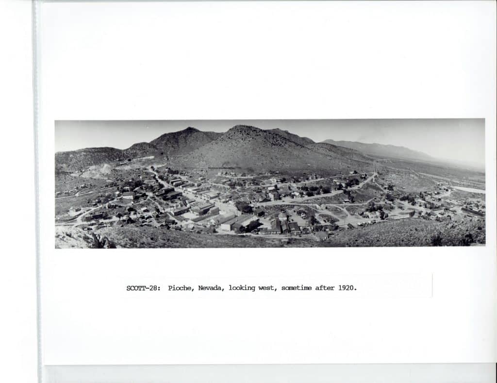 A black and white panoramic photo shows a small town nestled in a valley surrounded by arid mountains.