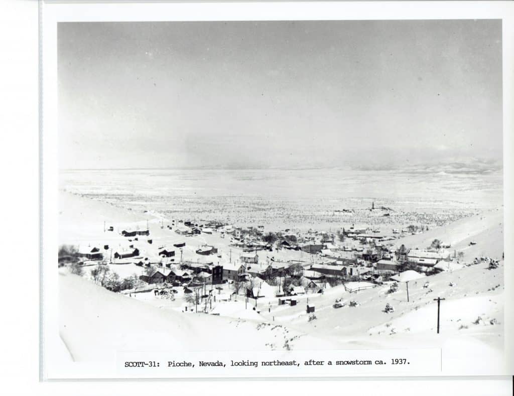 A black and white photo shows a snow-covered town in a valley, with "SCOTT-31: Pioche, Nevada, looking northeast, after a snowstorm ca. 1937" at the bottom.