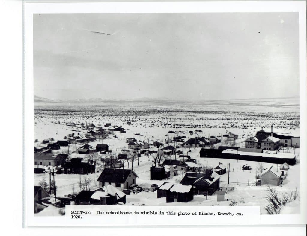 A black and white photo shows a snowy town with many houses and a vast, flat, snow-covered landscape.