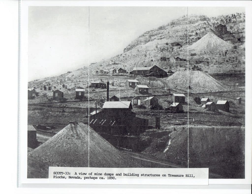 Black and white photo of a mining town with buildings and large dirt piles on a barren hillside.