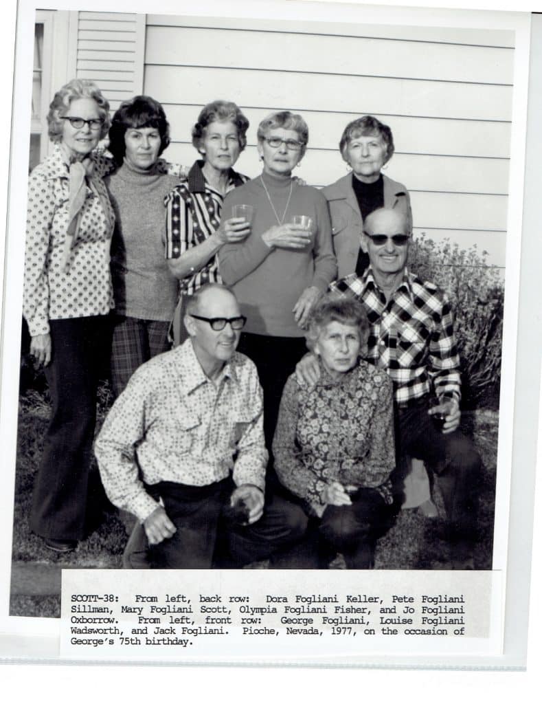 Nine people, six women and three men, pose for a group photo outdoors in front of a house.