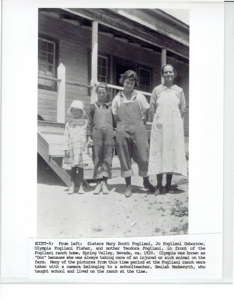 Four people, including a child in a hat and two women in overalls, stand on a porch.