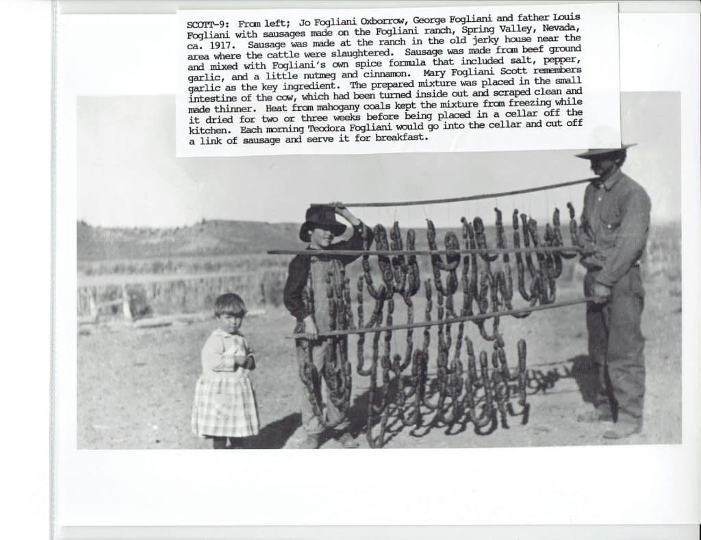 A man, a boy, and a girl stand next to a rack of hanging sausages in a black and white photo.