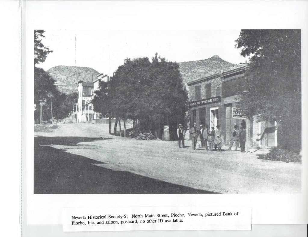 A black and white photo shows a dirt street with men standing in front of "BANK OF PIOCHE INC" and a "SALOON."