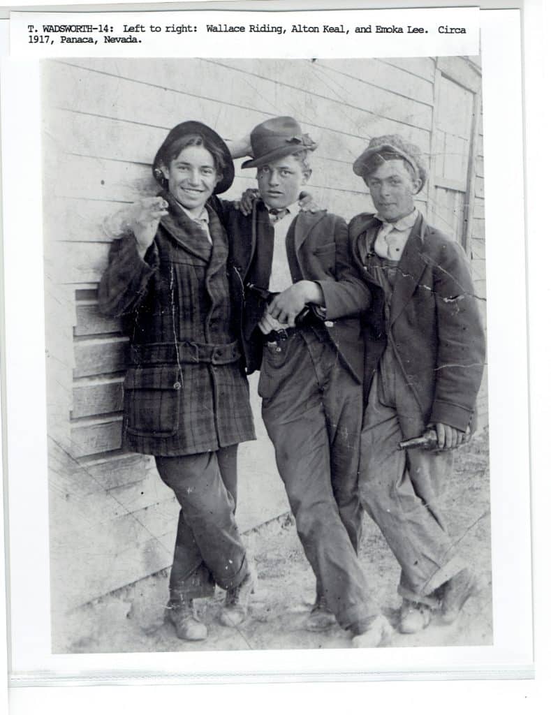 Three young men in hats and coats stand against a wooden building, with "T. WADSWORTH-14" text above.