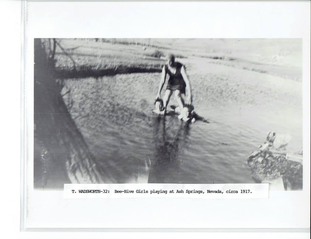 A black and white photo shows a person in a dark swimsuit playing with two children in a shallow stream.