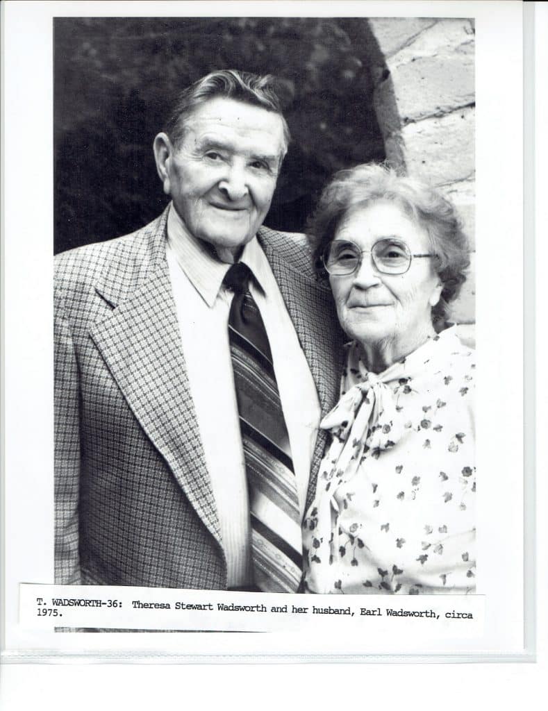 A black and white photo of an older man in a suit and a woman in glasses and a patterned blouse.