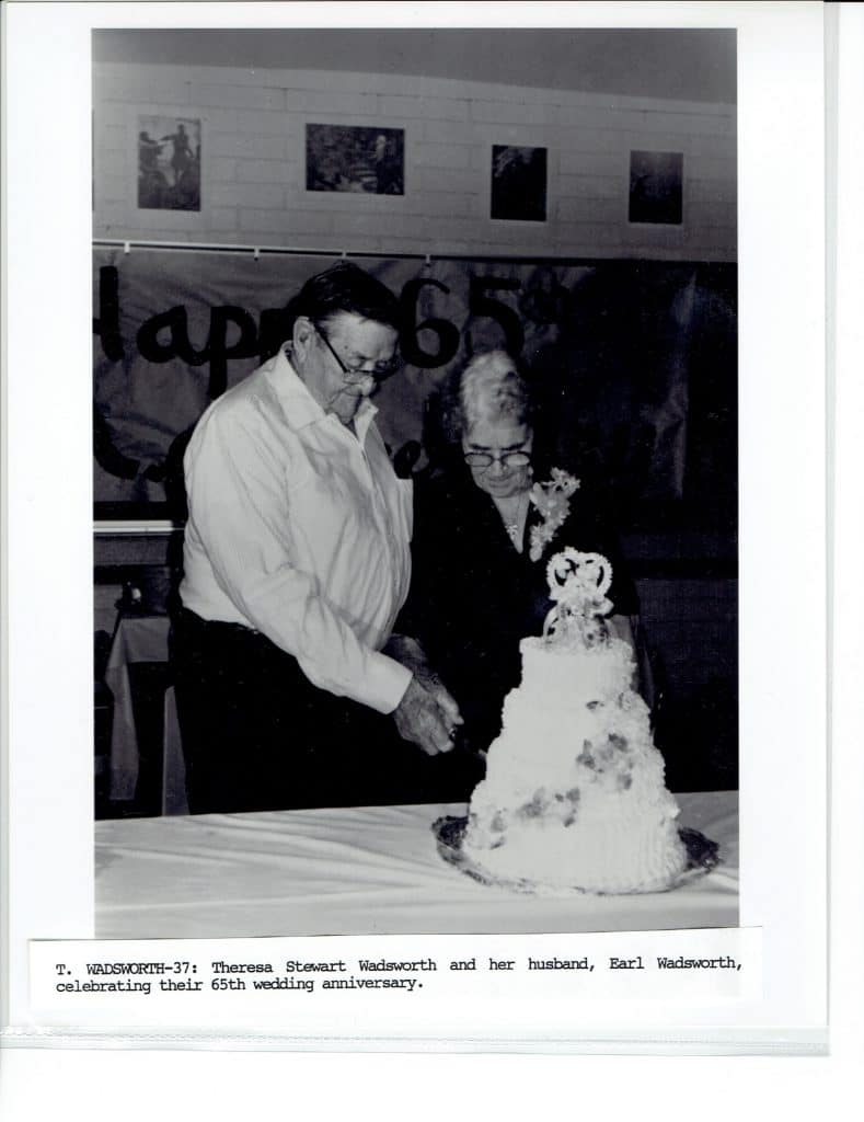 A black and white photo of a man and woman cutting a tiered cake, with "Happy 65" on a banner.