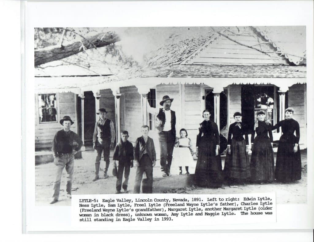 A black and white photo of ten people, six men and boys, four women and girls, standing in front of a house.