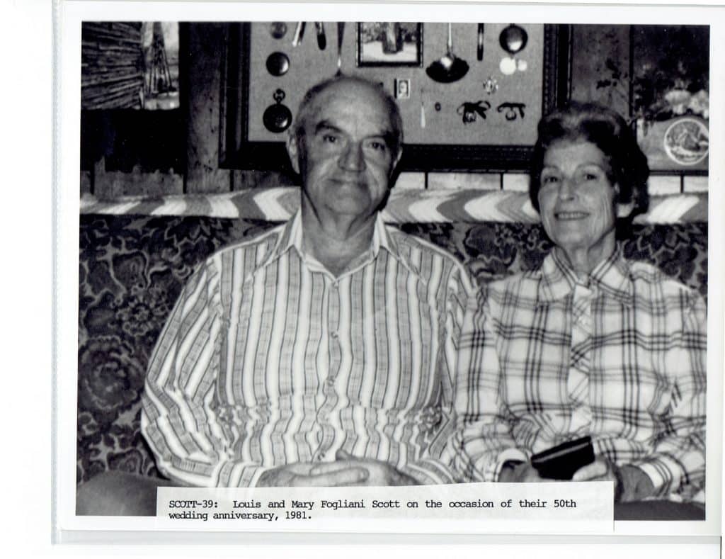 A smiling older man in a striped shirt and a woman in a plaid shirt sit on a patterned couch.